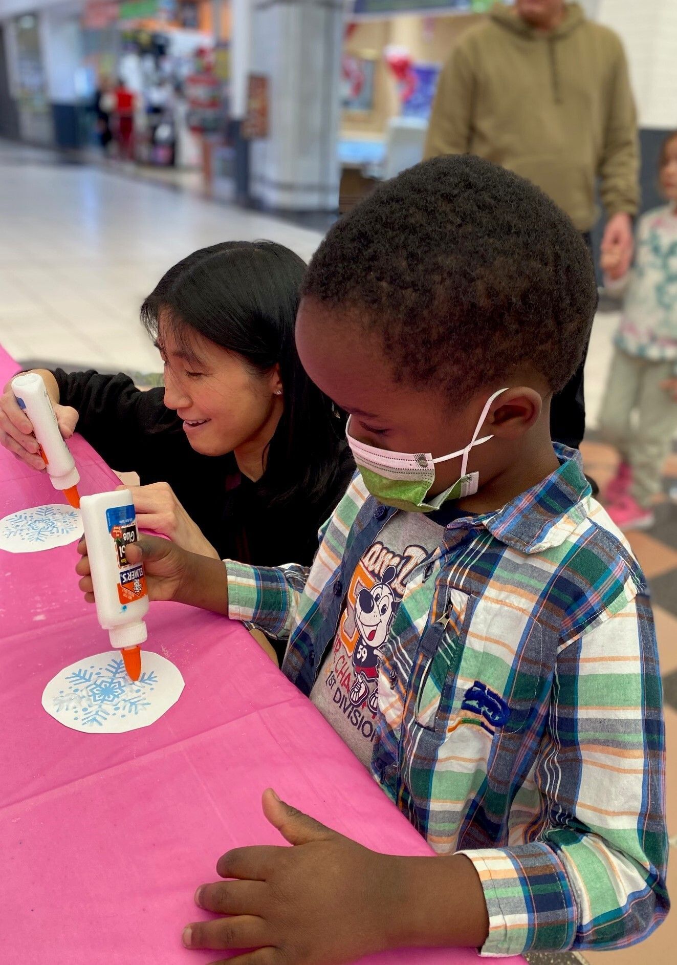 Two children putting glue on their paper snowflake art projects