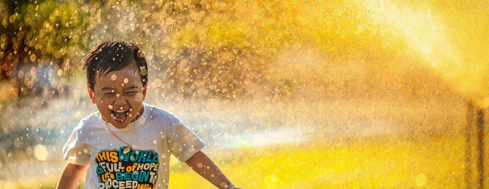 Child smiling and running through a water sprinkler.