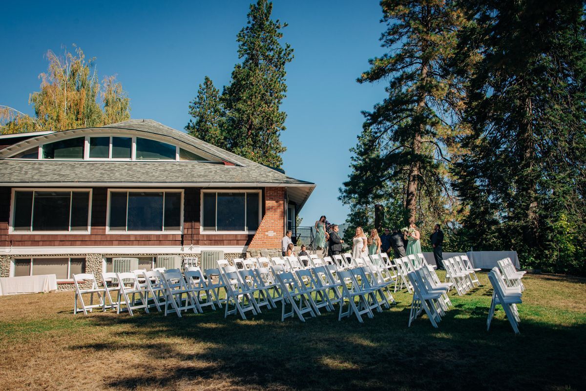 A scenic image of the lawn and the River Haus in the background, with white chairs set up in rows and people filing in to sit down.