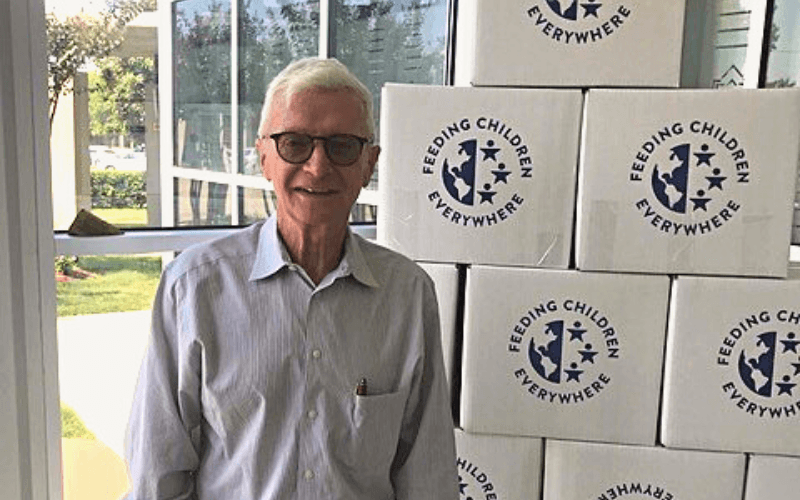 Charlie standing by a tower of boxes with meals for the needy