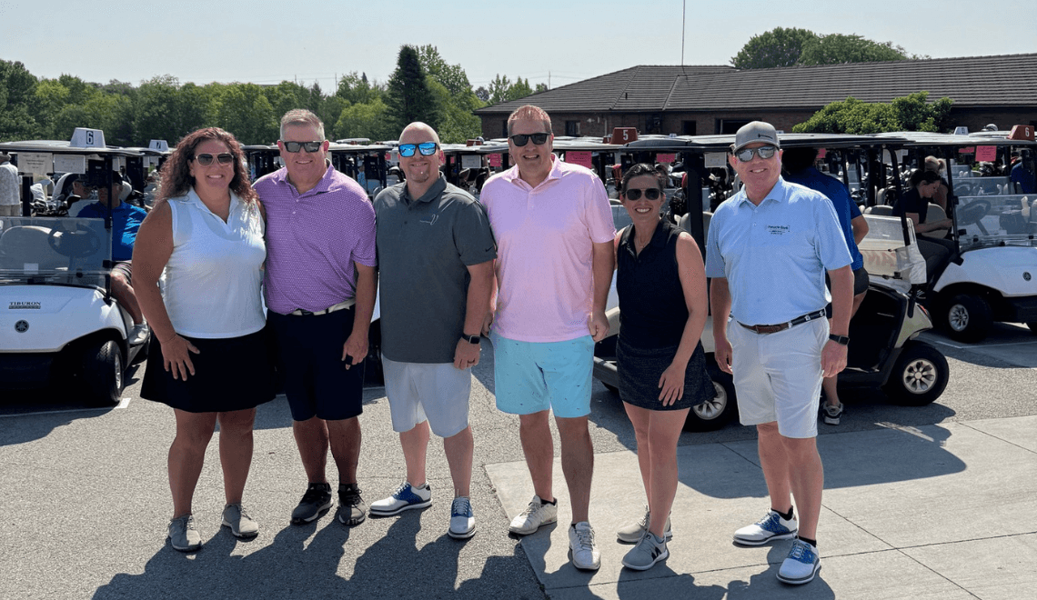 2025 golf committee in front of golfers in golf carts.