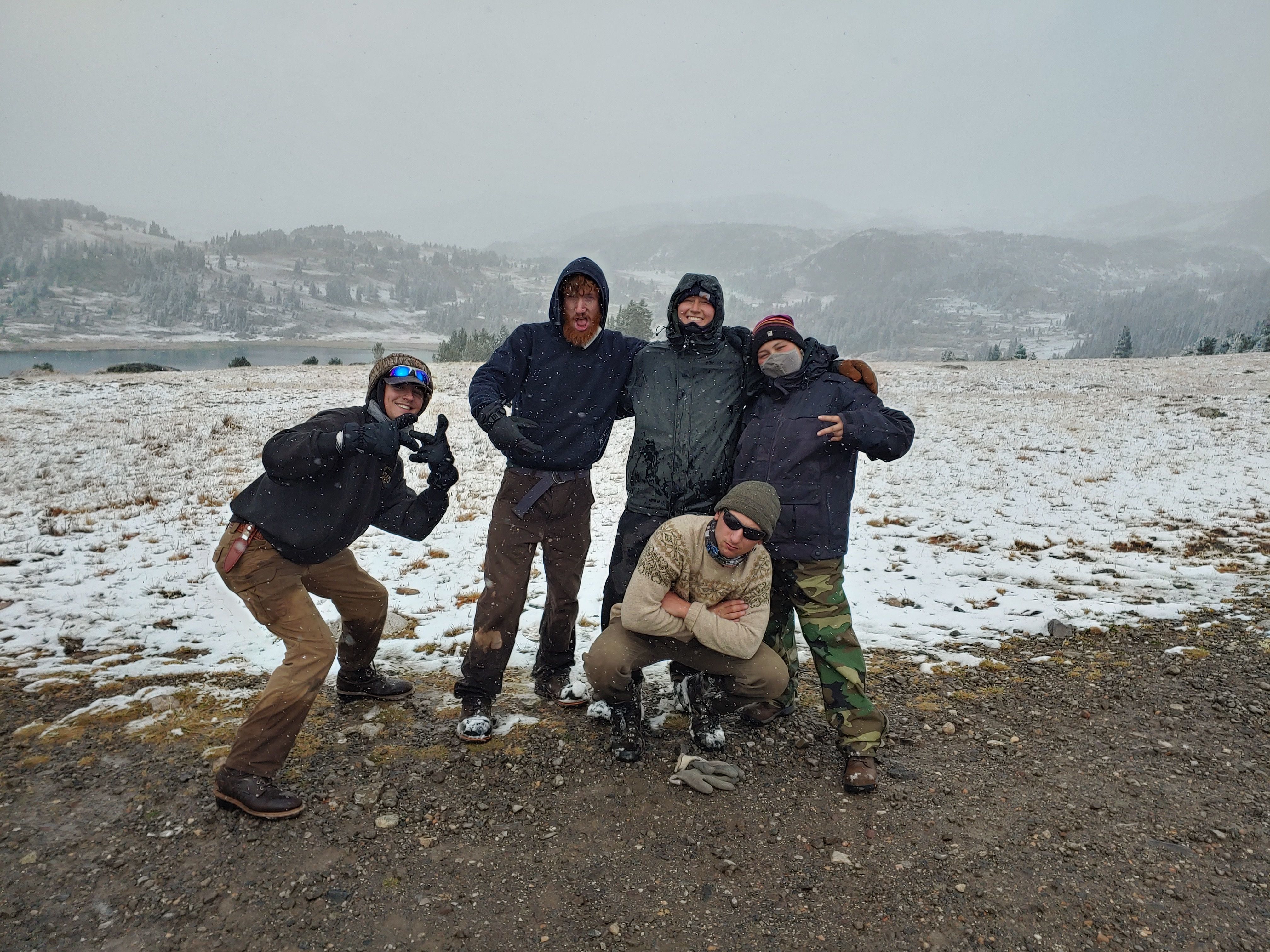 A crew poses, all bundled up in front of a snowy lake.