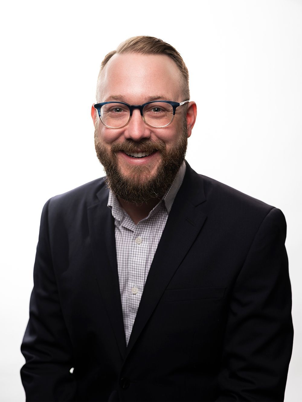 Chase Ghiloni is smiling in a professional headshot wearing a suit jacket, light blue button-up, and dark rimmed glasses.