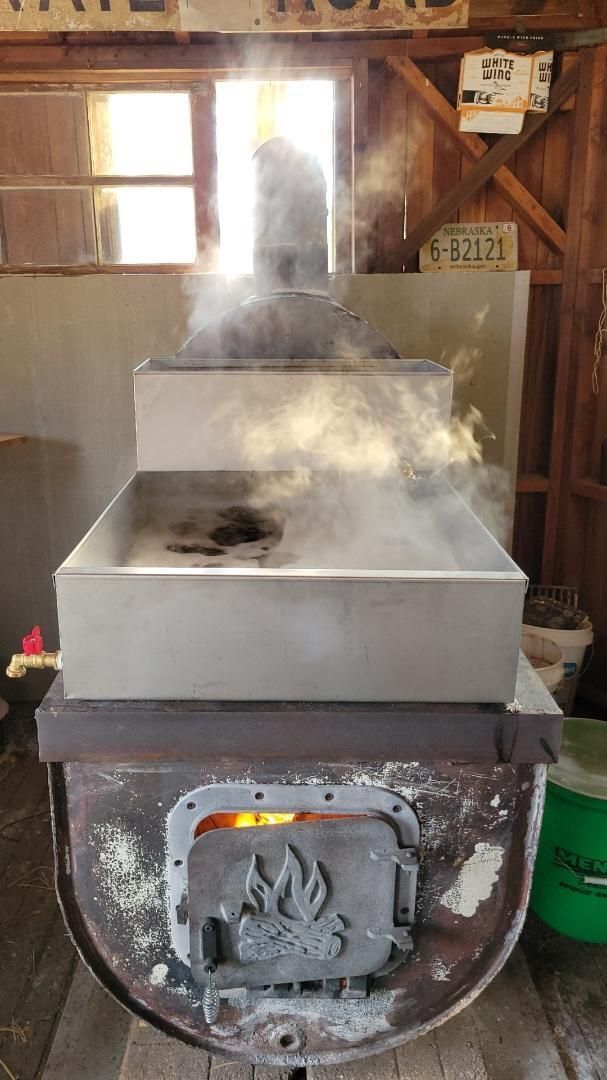 Syrup boiling in a large, square, metal box over a wood fire.