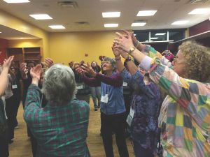 Women in a tight circle with their arms raised.