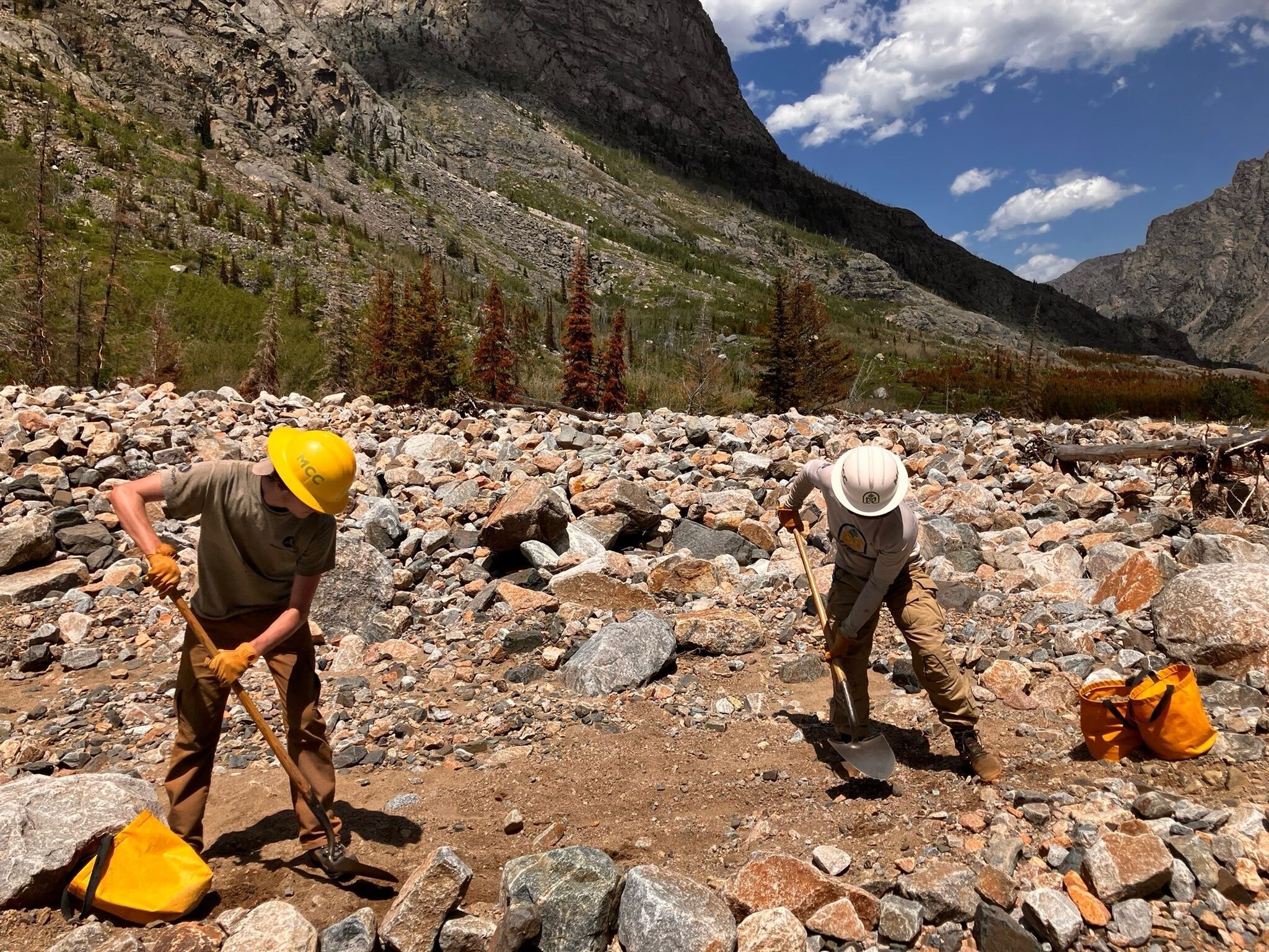 A crew member and a crew leader work to clear trail in a rock field