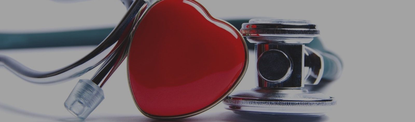 Closeup photo of a stethoscope and a bright red enamel heart. The heart is in the middle with the stethoscope's eartip to its left and the chestpiece on its right.