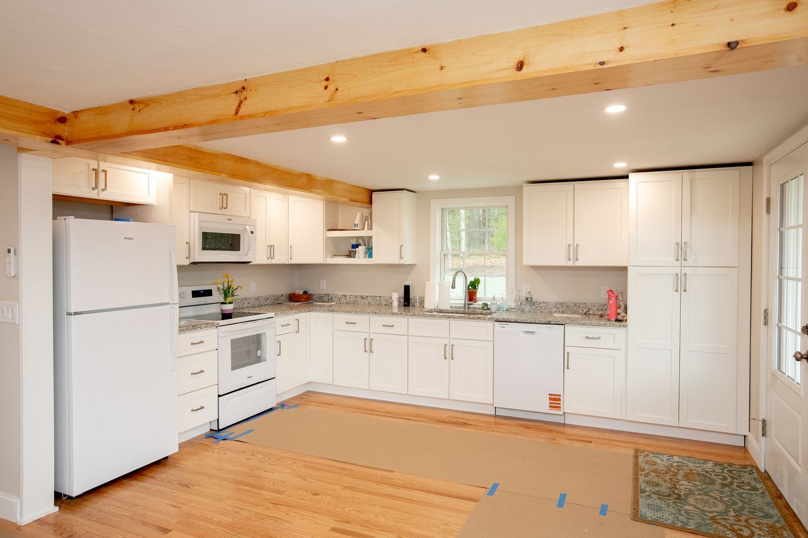 A photo of a completed kitchen with white cabinets, white appliances, and grey and black granite countertops