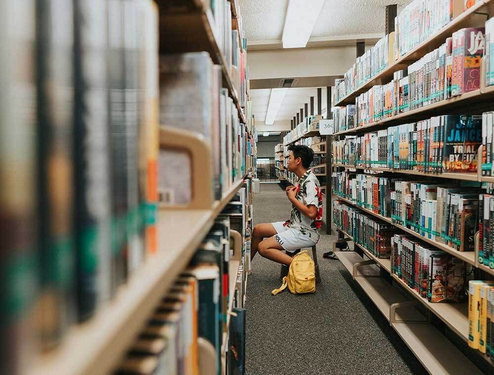 Person Looking for a Book on Library Shelf