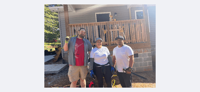 Three Arthrex volunteers standing and smiling in from of a Habitat Home under construction.