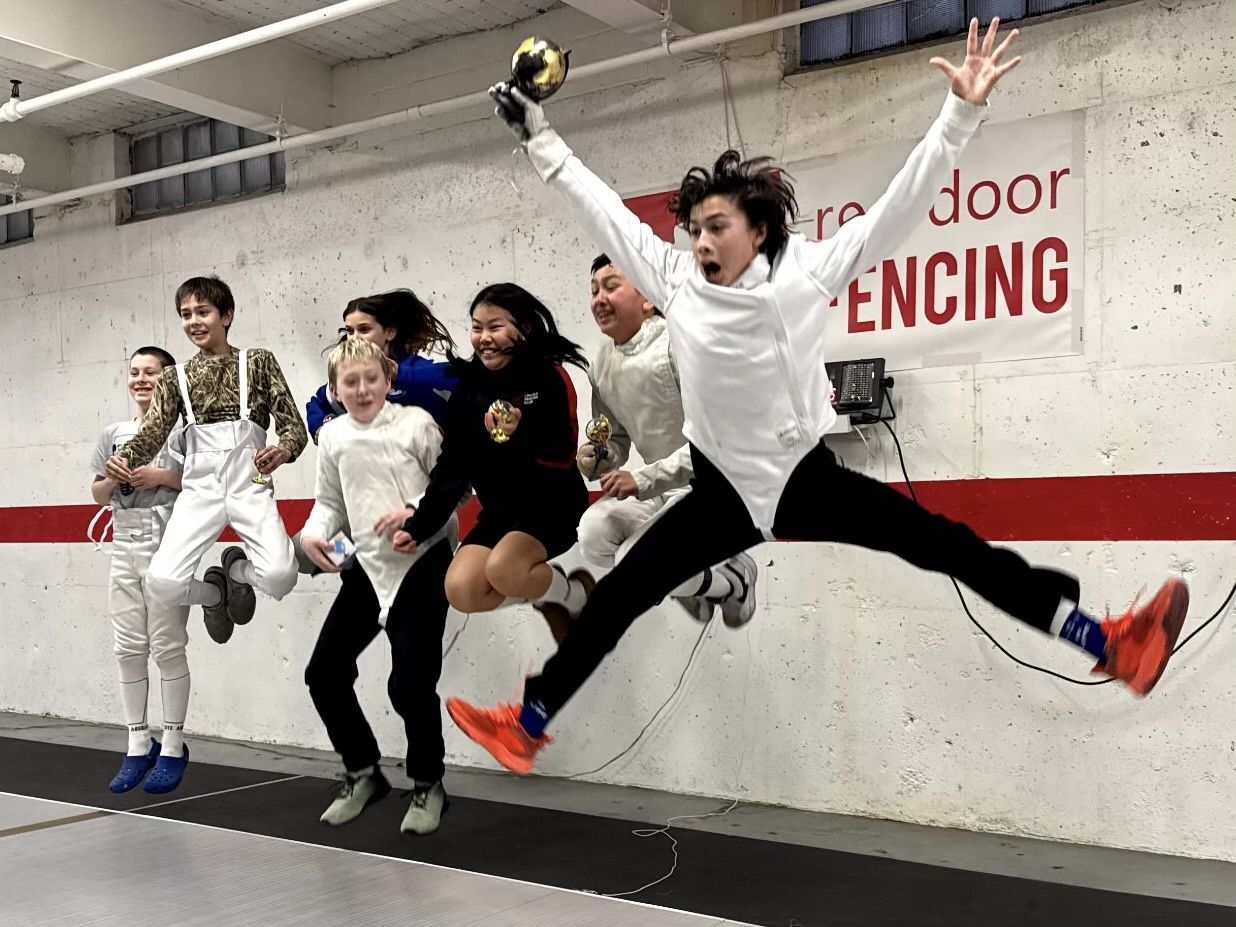 Youth fencers jump in the air holding their medals