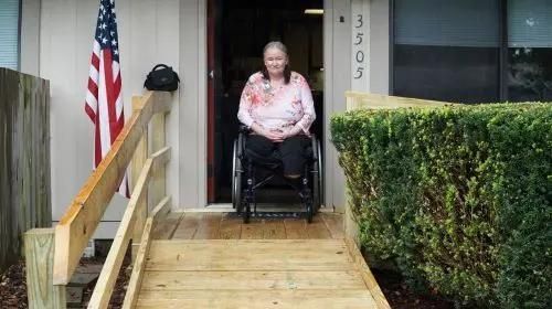 Woman in a wheelchair in front of her house.