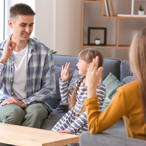 Father and daughter sign to each other with tutor looking on