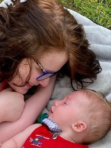 A mom and baby lay on a blanket on the ground facing each other