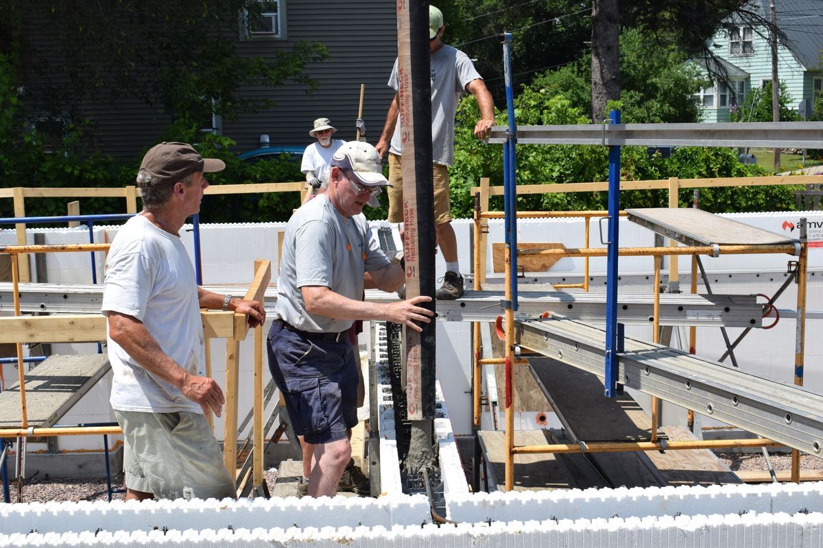 Volunteers help guide concrete into the foam insulation blocks.