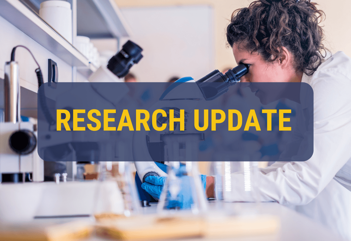 The image shows a scientist using a microscope in a laboratory setting, with a text overlay that reads "RESEARCH UPDATE" in bold, yellow letters. The background is slightly blurred, highlighting the focused work of the scientist.