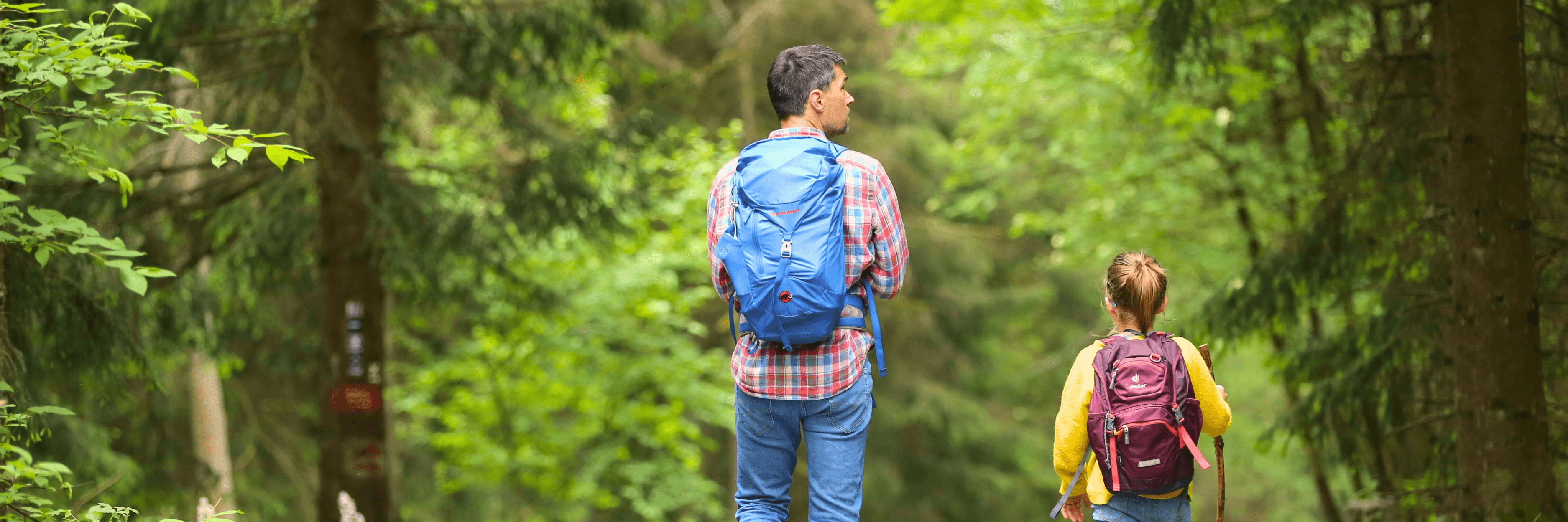 Father and daughter hiking together through forest with backpacks