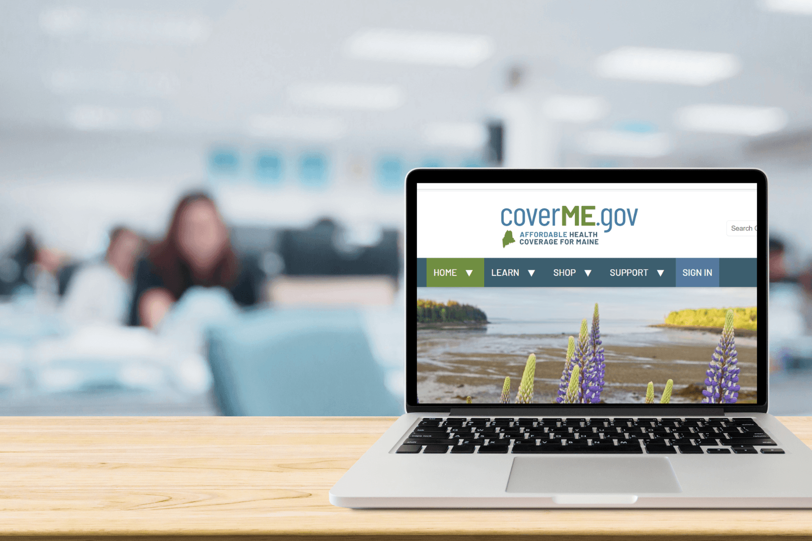 An open laptop in the foreground displays the CoverME.gov website while CAHC HelpLine advocates enroll in Marketplace health coverage in the background