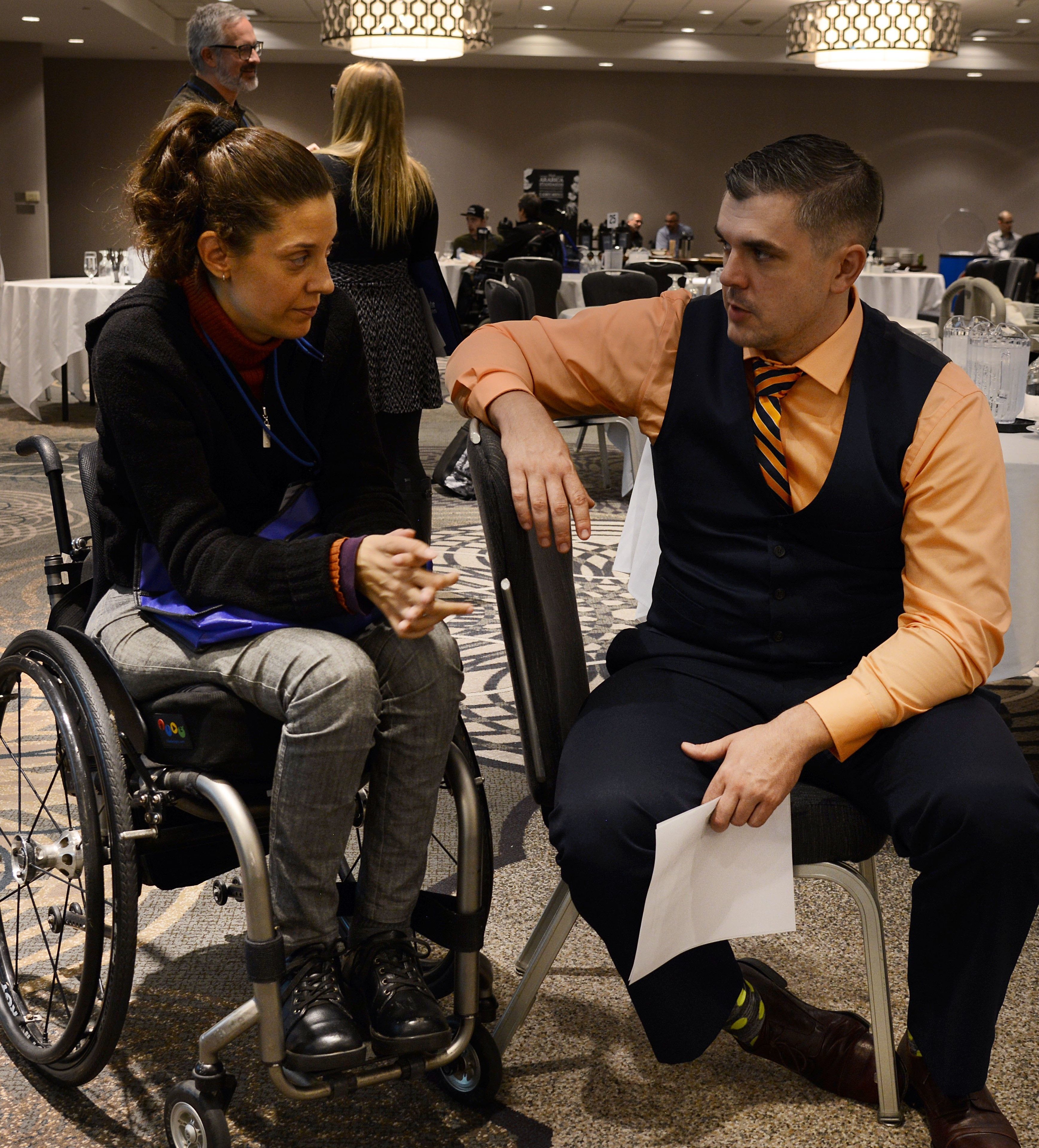 Woman in a wheelchair speaking with a man on a chair to her right