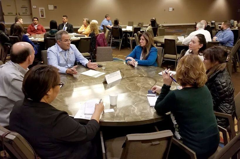 A group of people sitting around a large round table in a meeting.