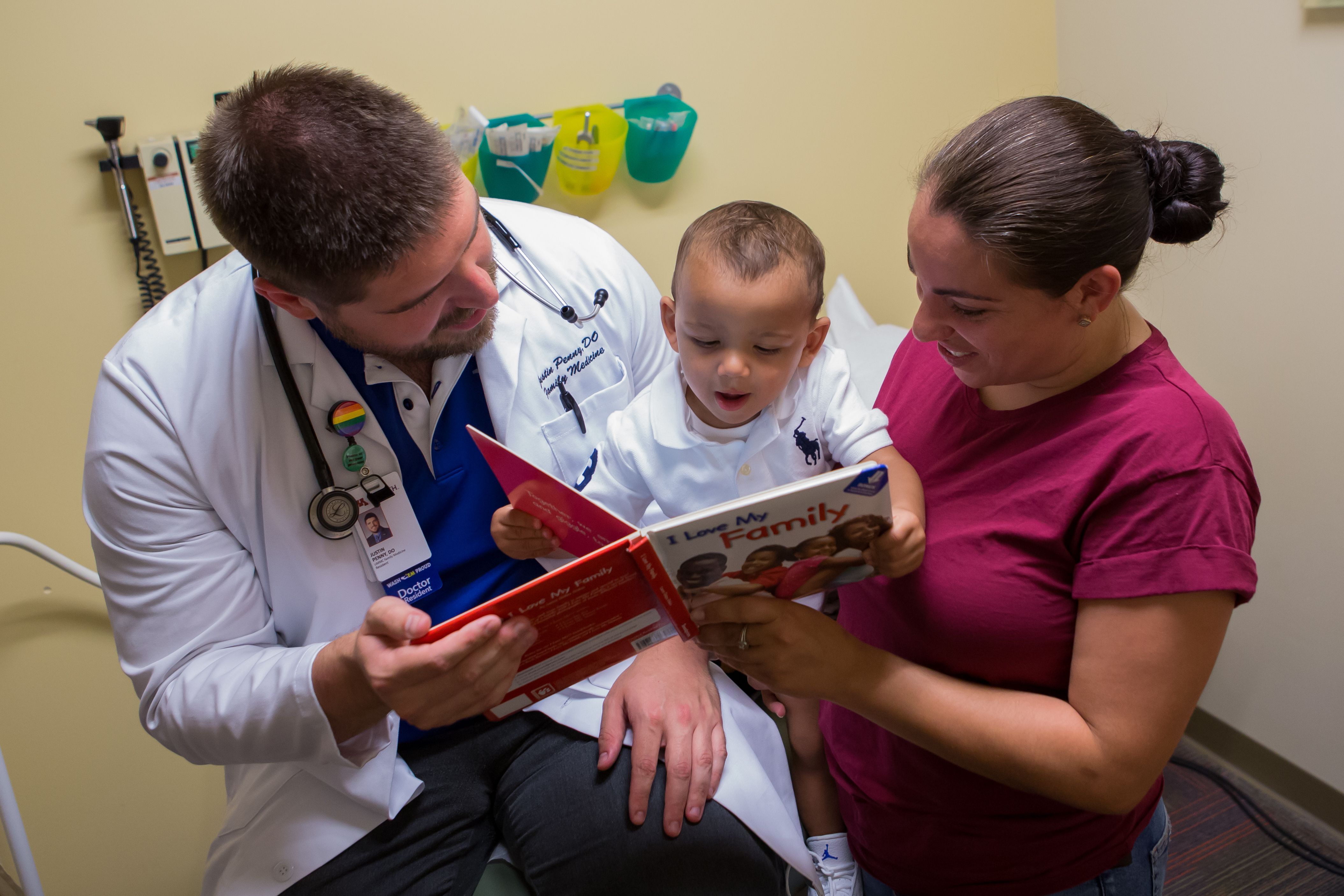 pediatrician,  toddler boy, and mother smile while sharing a book