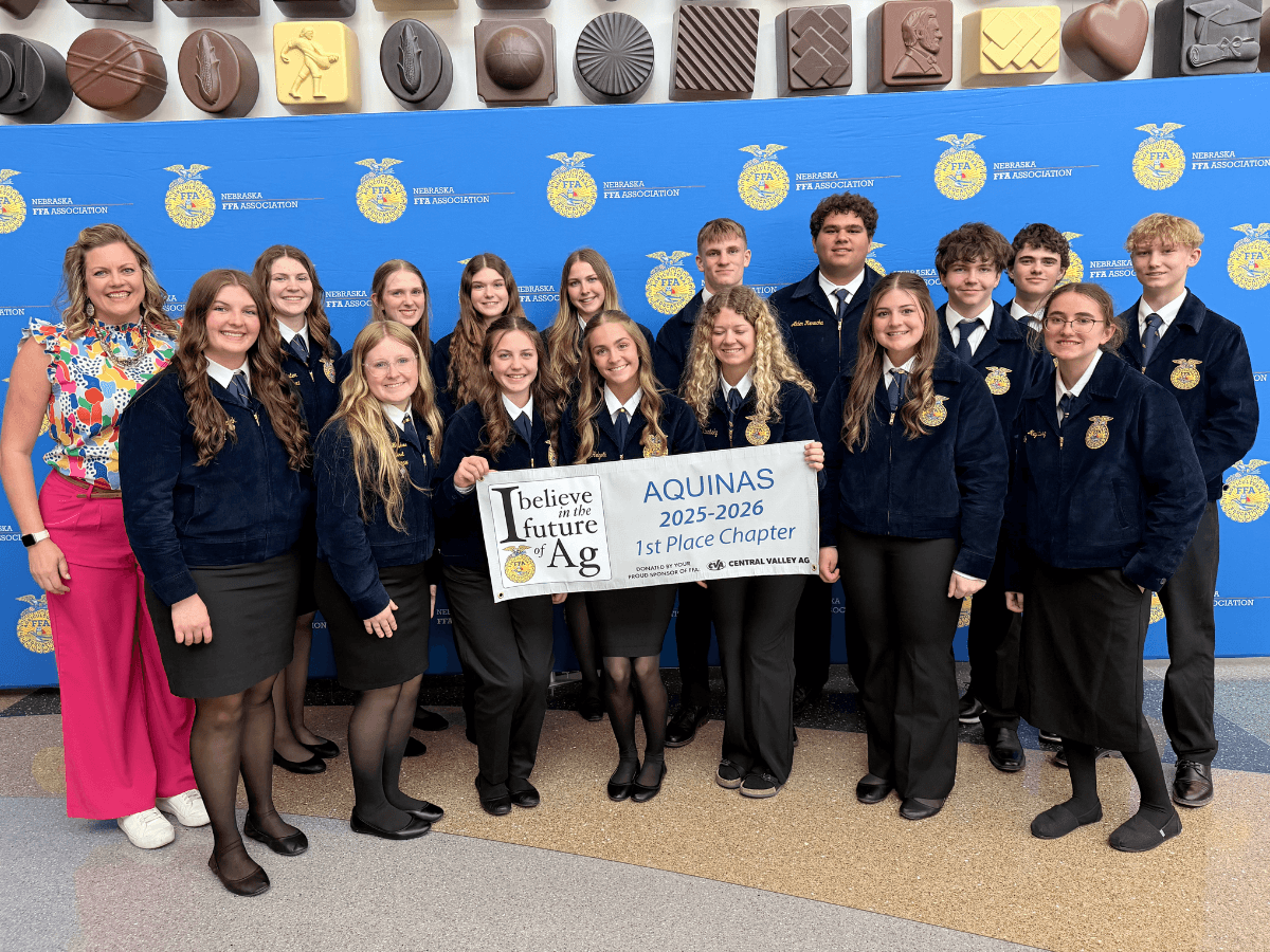 A teacher poses with a group of Aquinas FFA students holding a banner for first place.