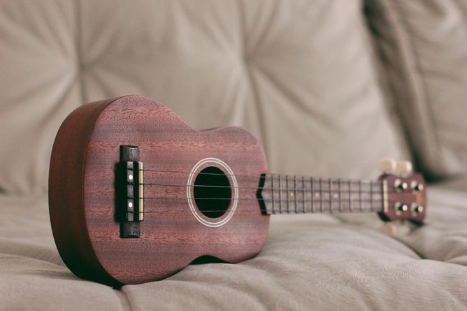 A soprano ukulele laying on its side on a couch.