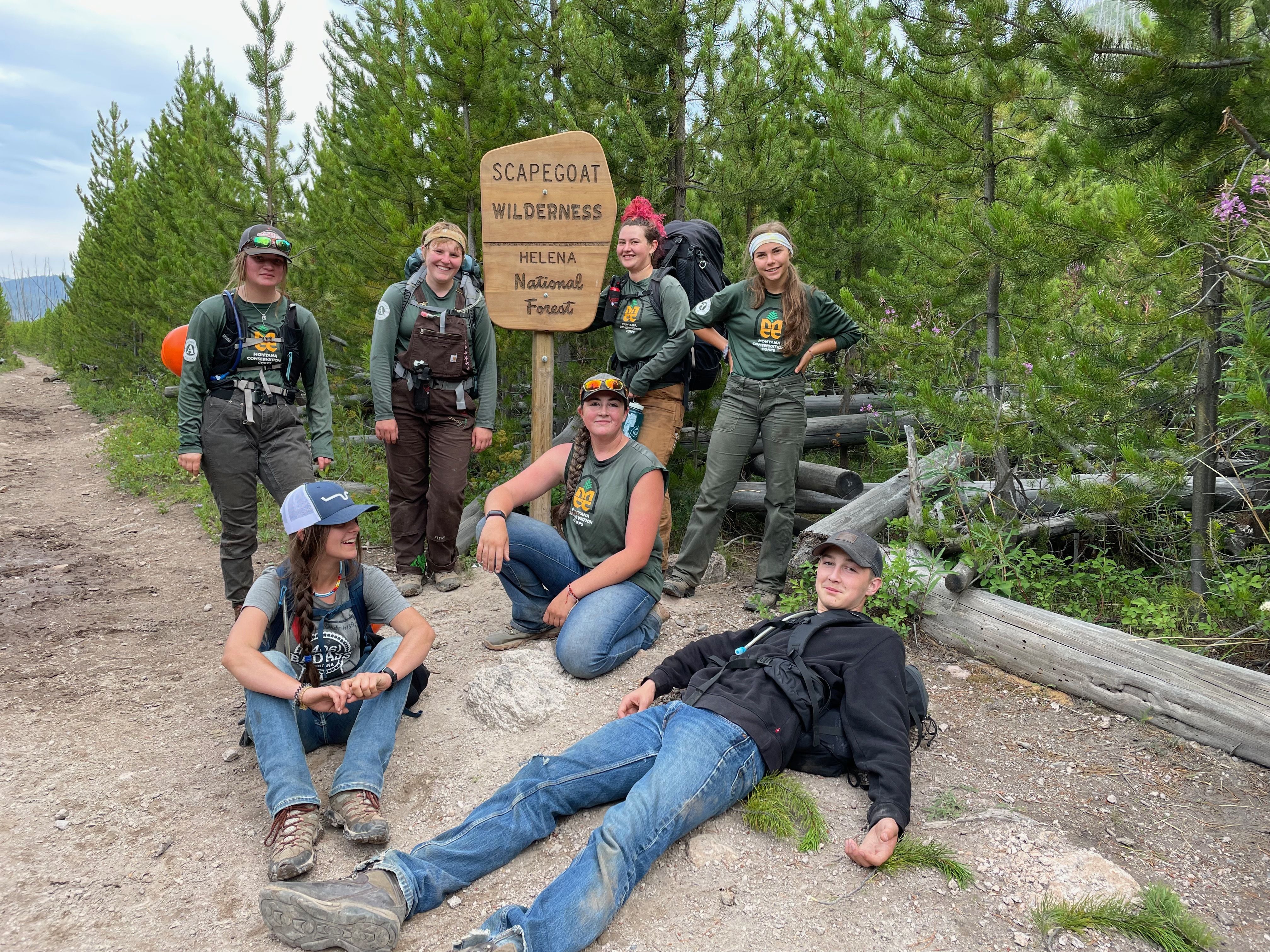 Two crew leaders and a youth crew stand by a wooden "Scapegoat Wilderness" sign