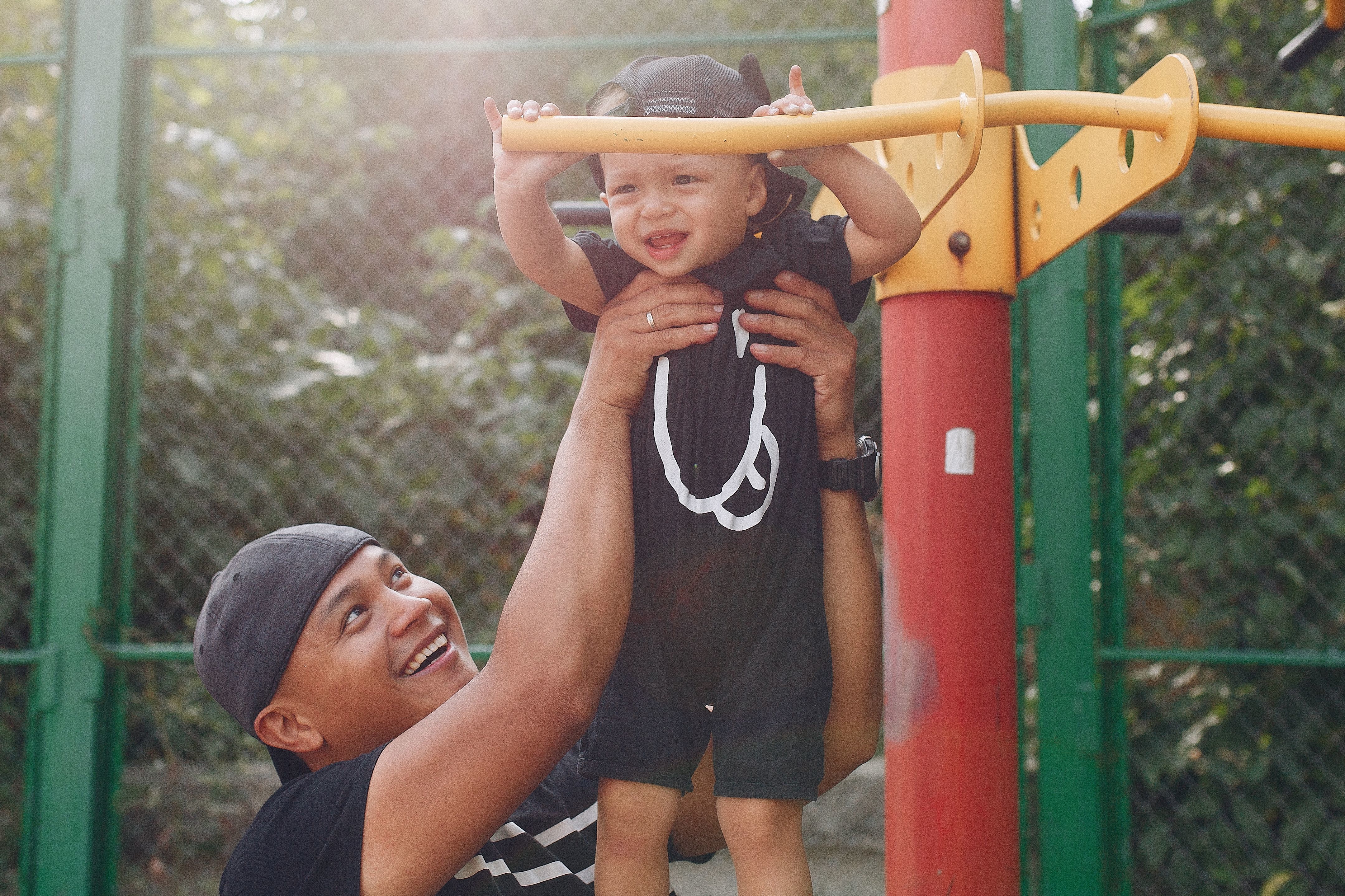 A father holding up a young boy at a playground.