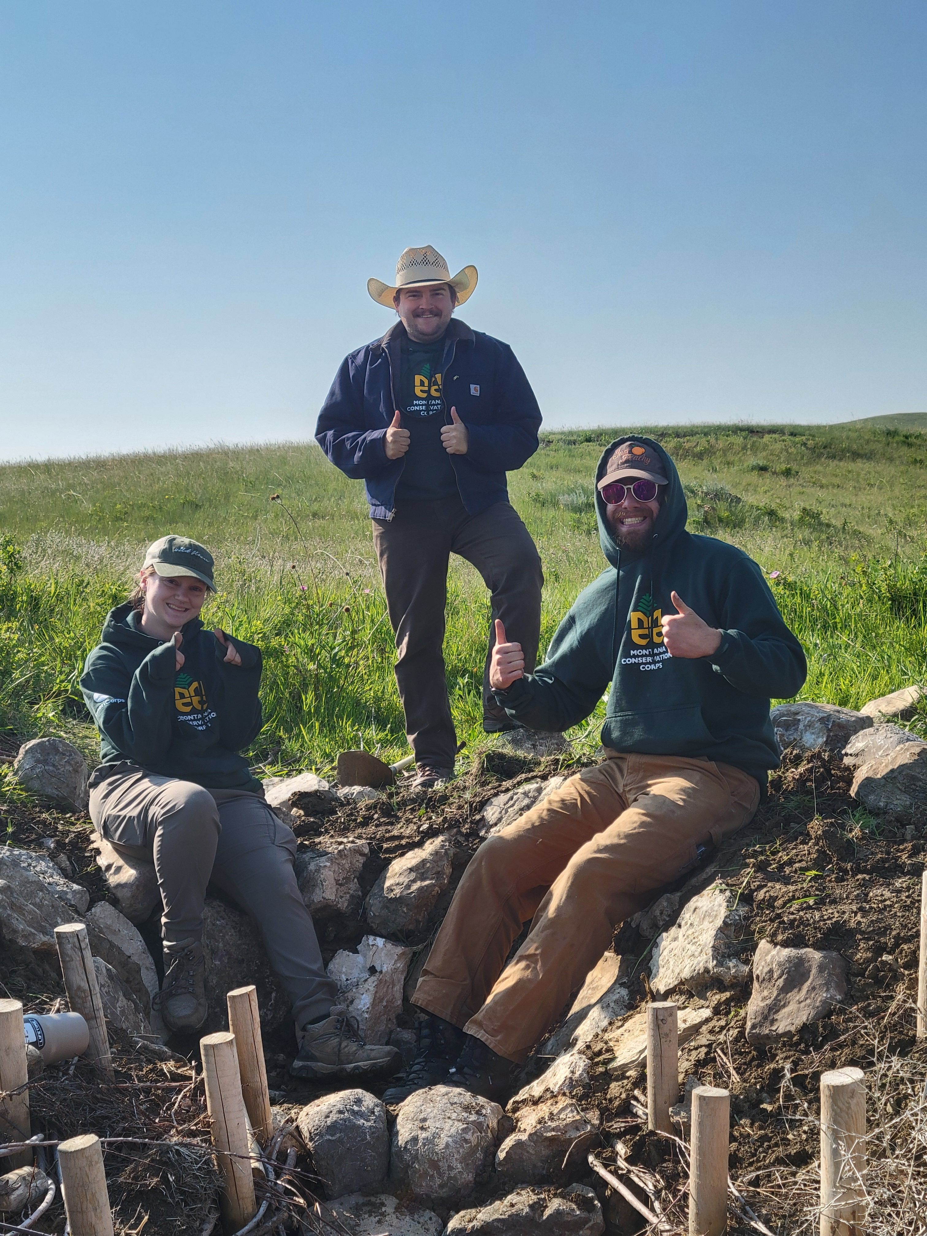 A crew sits and smiles next to a Beaver Dam Analog that they built.