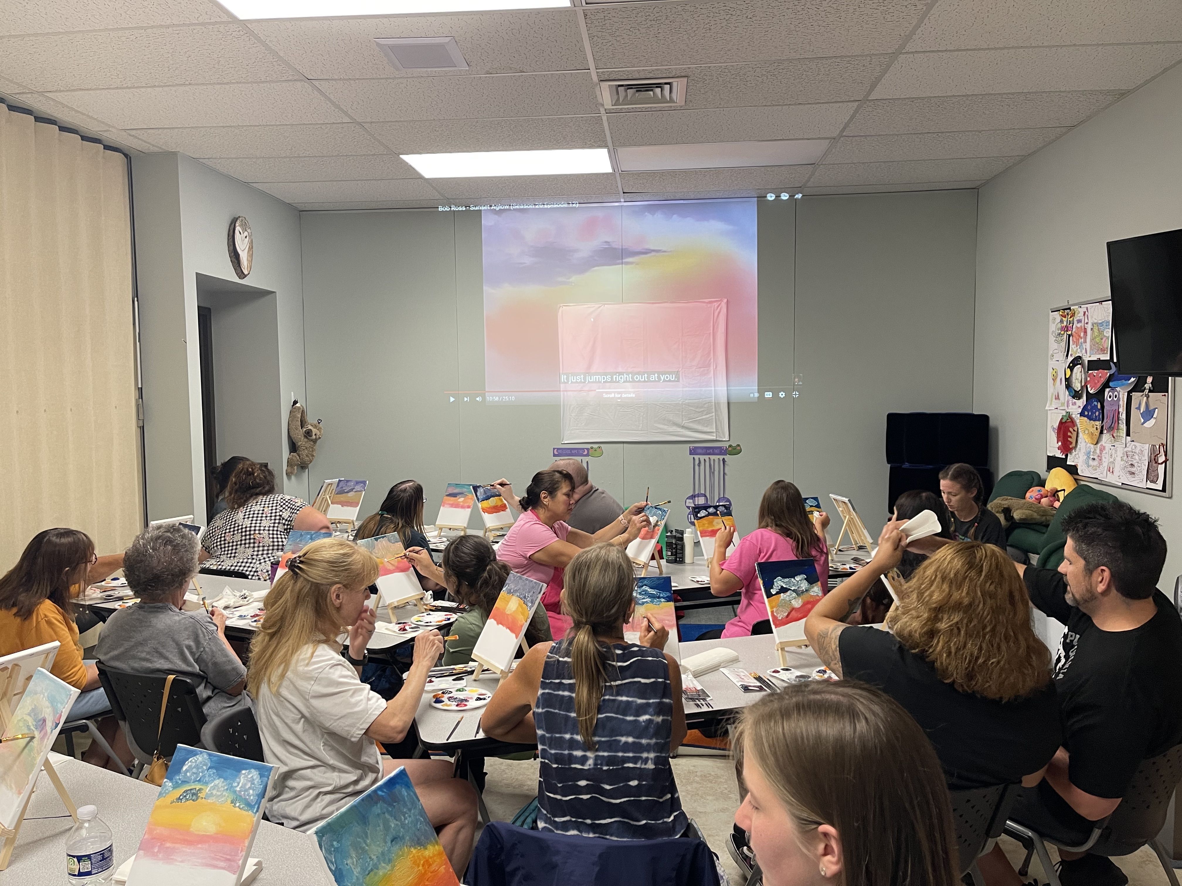 A photo of adults painting along with a Bob Ross tutorial