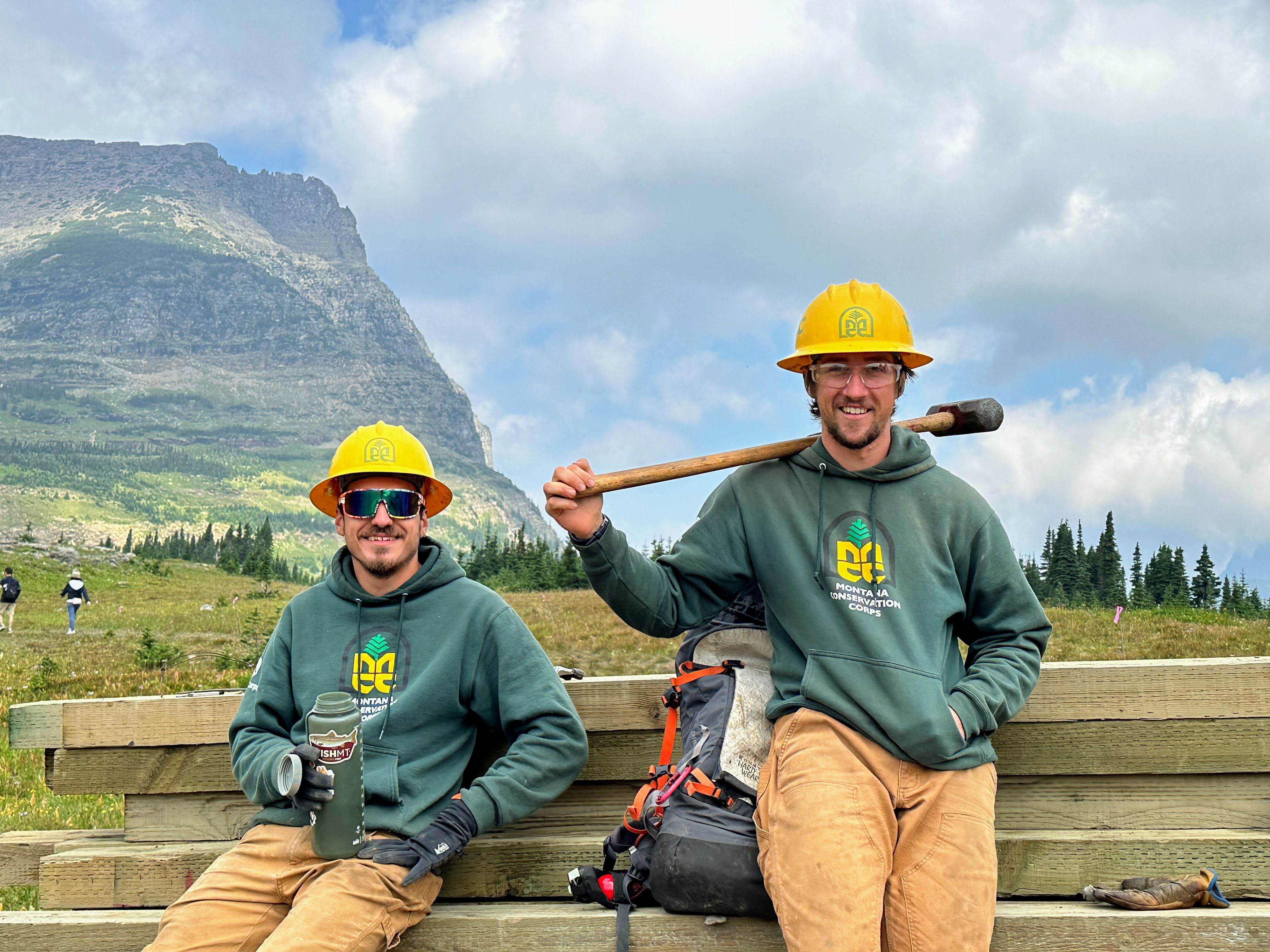 Two crew members lean against a pile of boardwalk planks