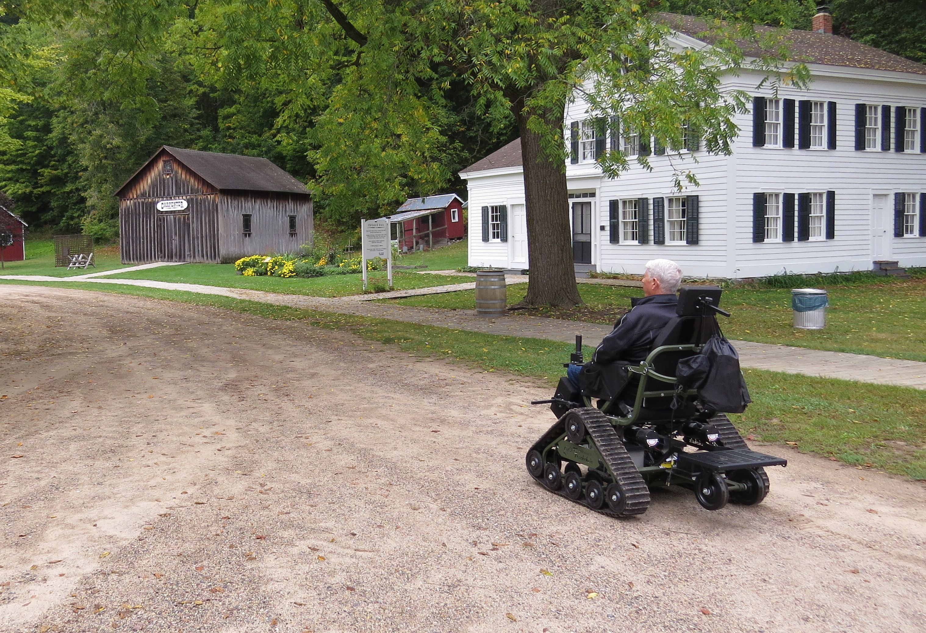 Person using the track chair and traveling through the historic village on a summer day.