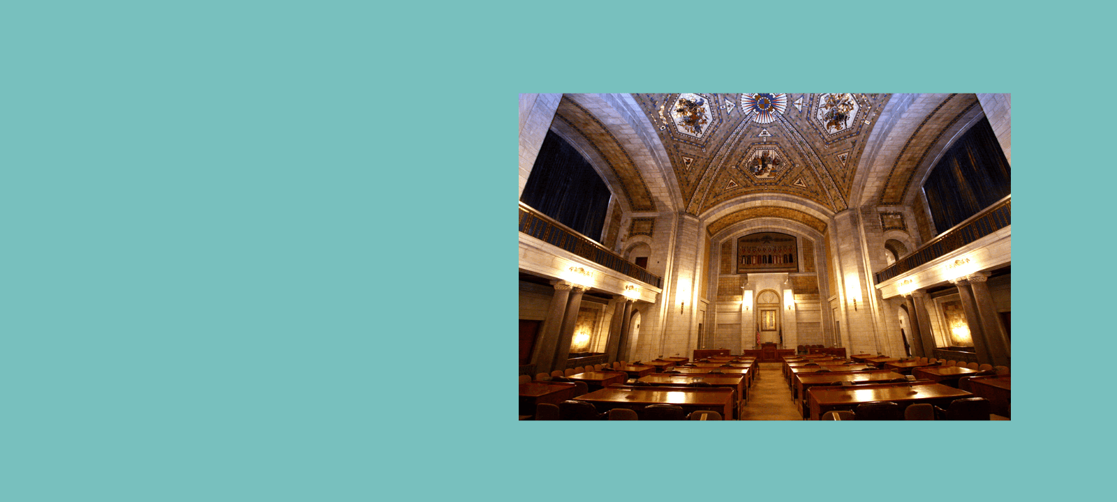 Warner Chamber at the Nebraska Legislature. Room has rows of desks that seat two people each. Mosaic ceiling and brick walls