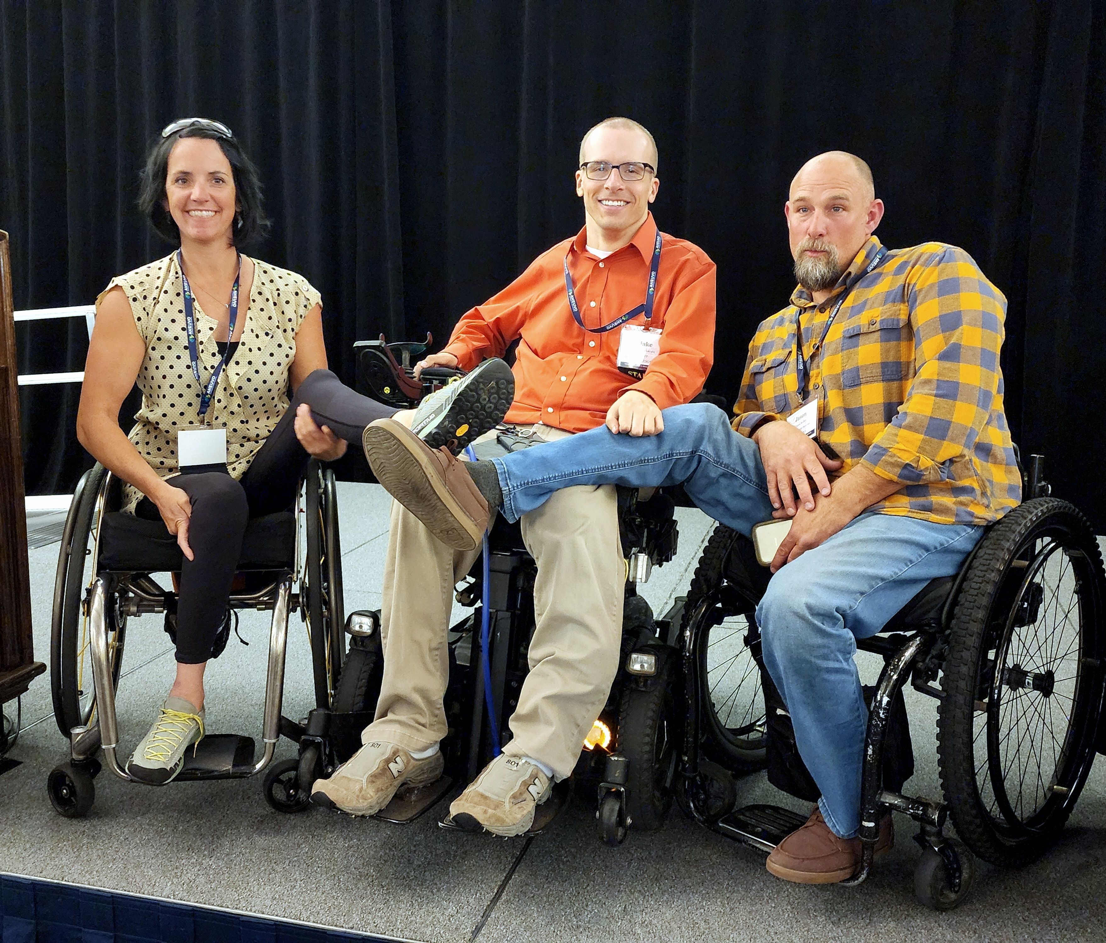 A woman and two men in wheelchairs smile at the camera together