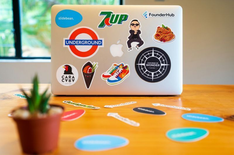 Laptop and desk covered with custom die cut stickers from startups and brands, showing playful, layered sticker marketing display.