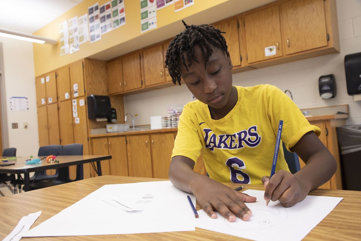 young boy drawing at desk wearing a yellow Lakers shirt 