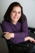 Ann Marie Morelli, Administrative Associate/Research and Development. A women who is wearing a purple shirt crossing her arms. She is sitting in a power wheelchair smiling for the picture.