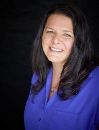 White woman with mid-chest length hair standing in front of a tree