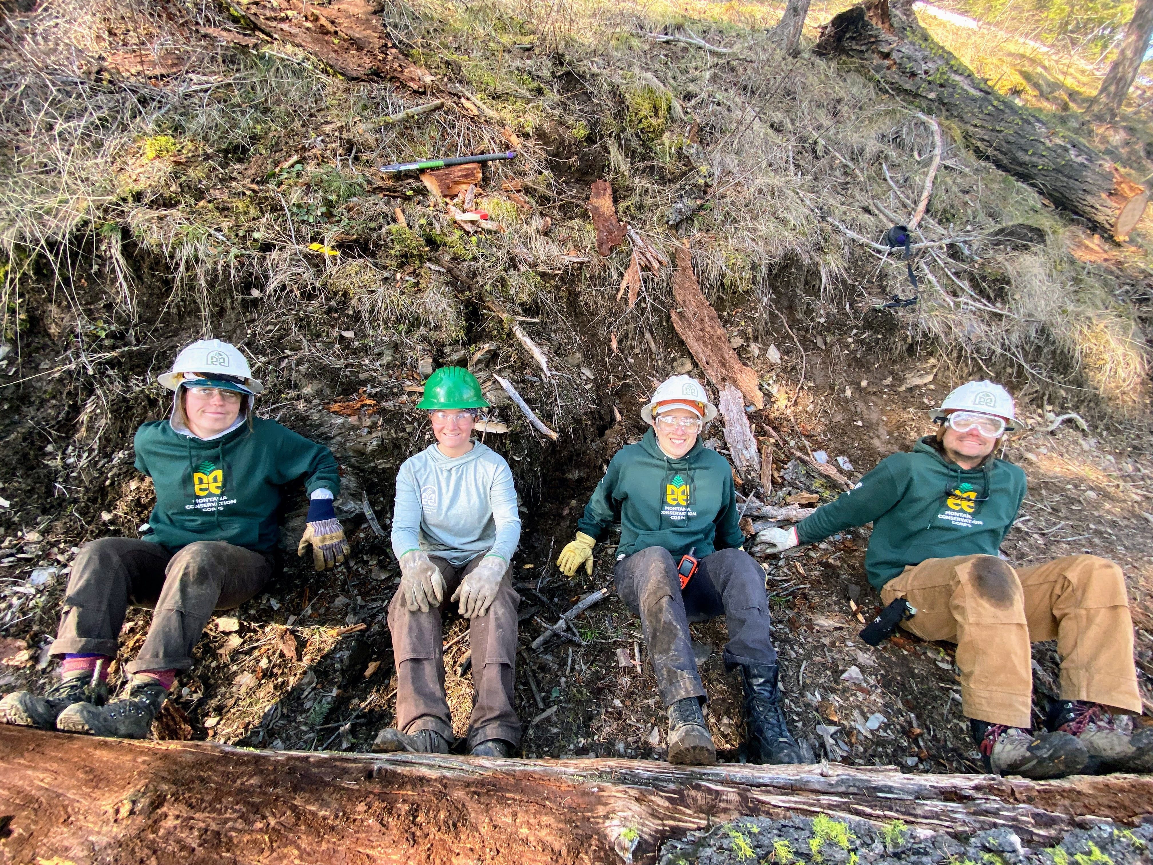 Three crew leaders and one MCC staff member sit by a log they are about to push off the trail.