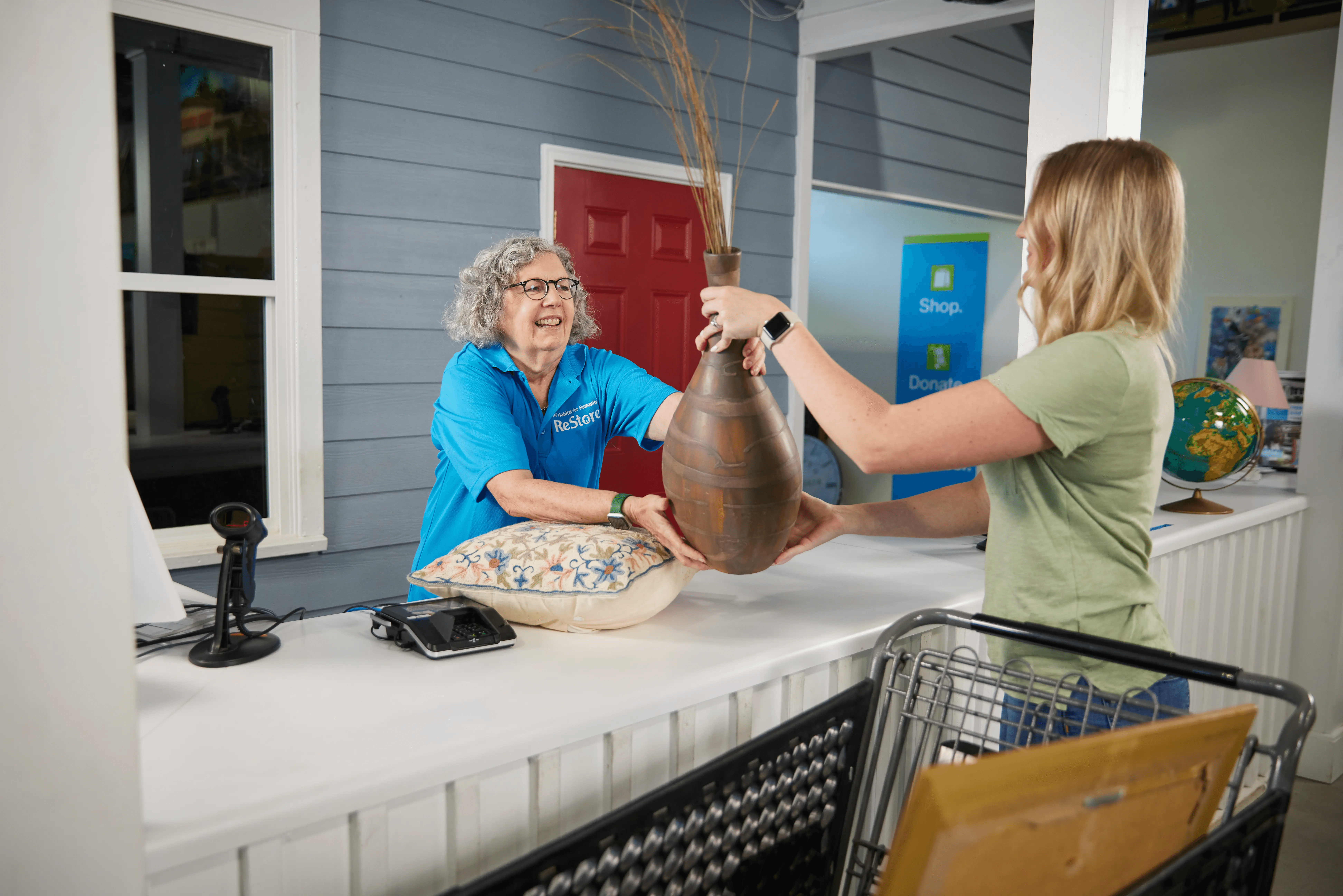 Habitat ReStore volunteer assisting a customer with a donated home decor item at the checkout counter, showing how shopping and donating help build affordable homes in Pasco County.