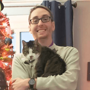 Young man holding a cat in front of a Christmas Tree