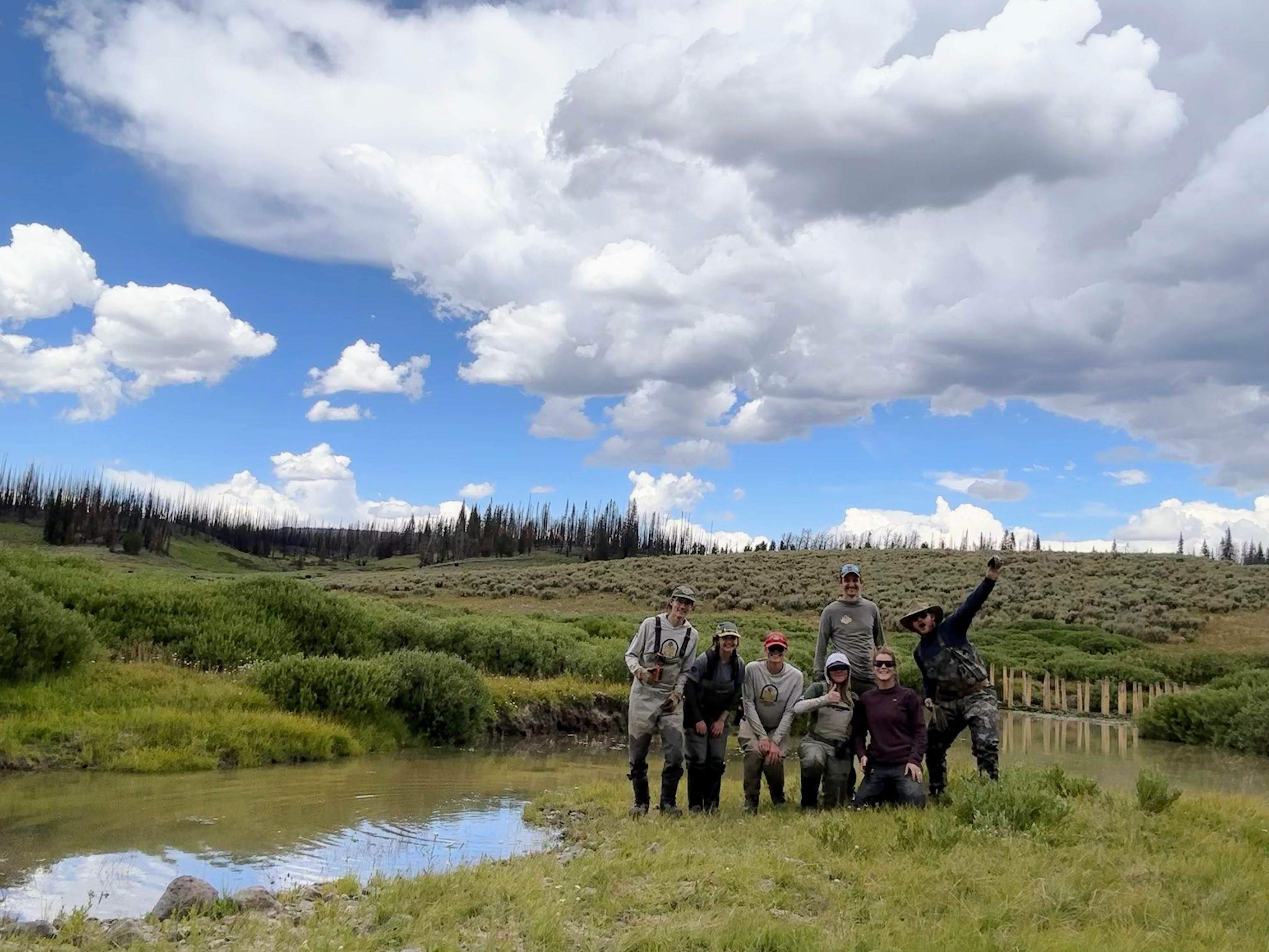 A crew stands next to a small creek and a BDA structure.