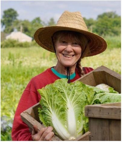 A woman in a wide-brimmed straw hat smiles at the camera while holding a huge tall head of lettuce