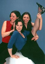 BRECHT ON BRECHT - 2002. A group of women that are having a great time. One person is wearing a red shirt. The second person is wearing a blue shirt and she has her leg in the air. The last person is wearing a black dress. They are posing for the photo. 