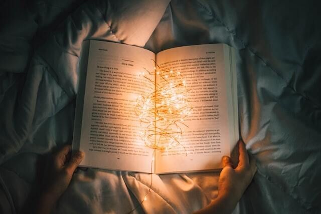 Hands holding a book open with bright lights illuminating the pages