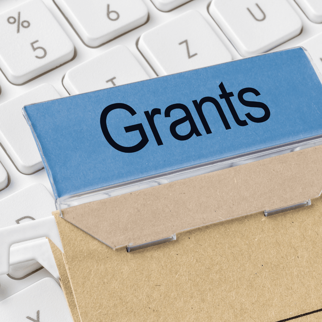 Photo features a folder marked grants sitting on top of a computer keyboard