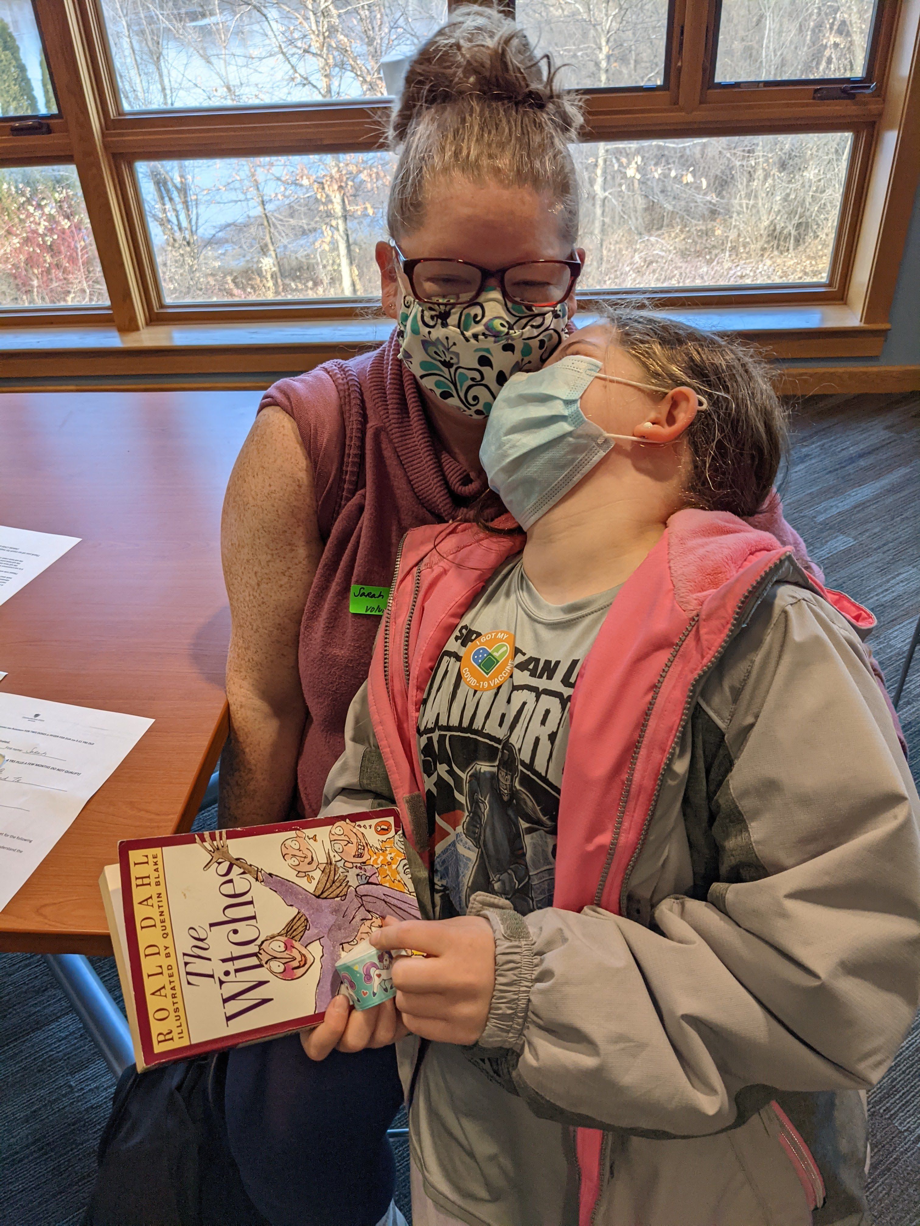 Girl and her mother enjoy a book received at COVID-19 vaccination 