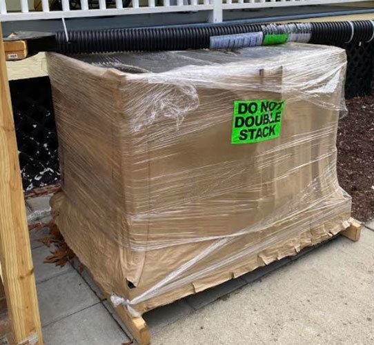 Disassembled wheelchair lift shipped. The platform is wrapped in cardboard and the lift column is in some ribbed tubing.