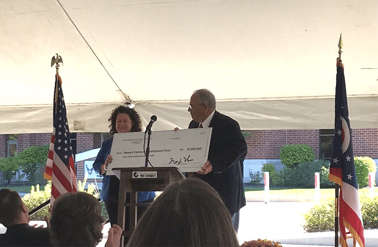 A short women presents a ceremonial giant check to an older gentleman.